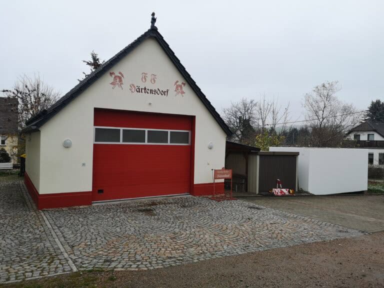 Feuerwehrhaus mit großem roten Garagentor und Einfahrt davor