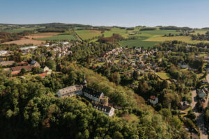 Vogelperspektive über dem Ort Wildenfels. Es sind Grünflächen, Häuser und das Schloss Wildenfels zu sehen