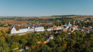 Vogelperspektive über dem Ort Wildenfels. Es sind Bäume, Häuser und das Schloss Wildenfels zu sehen
