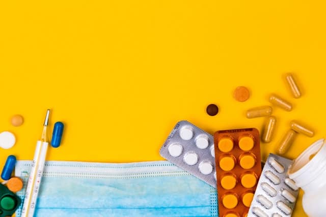 Auf dem Bild sind Tabletten, Kapseln, ein Fieberthermometer und eine Maske zu sehen