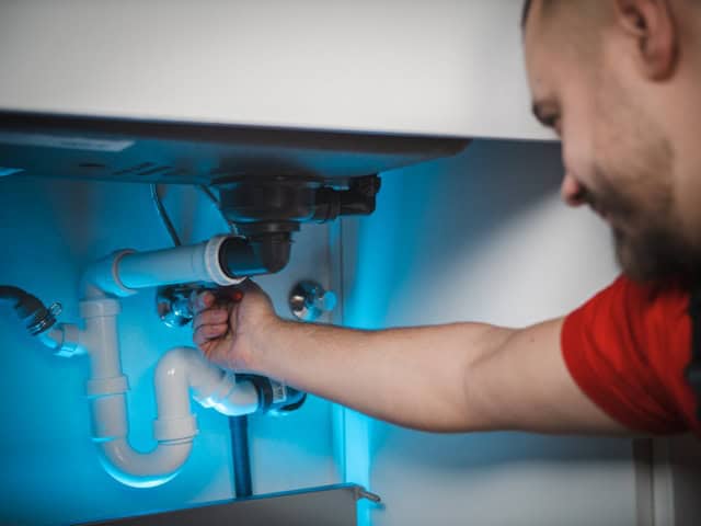 Auf dem Bild arbeitet ein Klempner an den Rohren unter einem Waschbecken